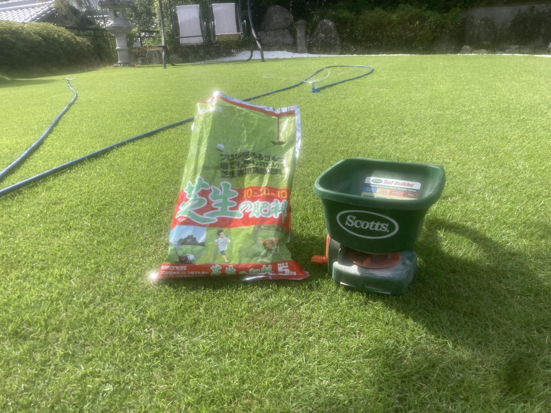 芝生の上に置かれた肥料袋と手動散布機。真夏の施肥作業中のYASUYO庭の様子